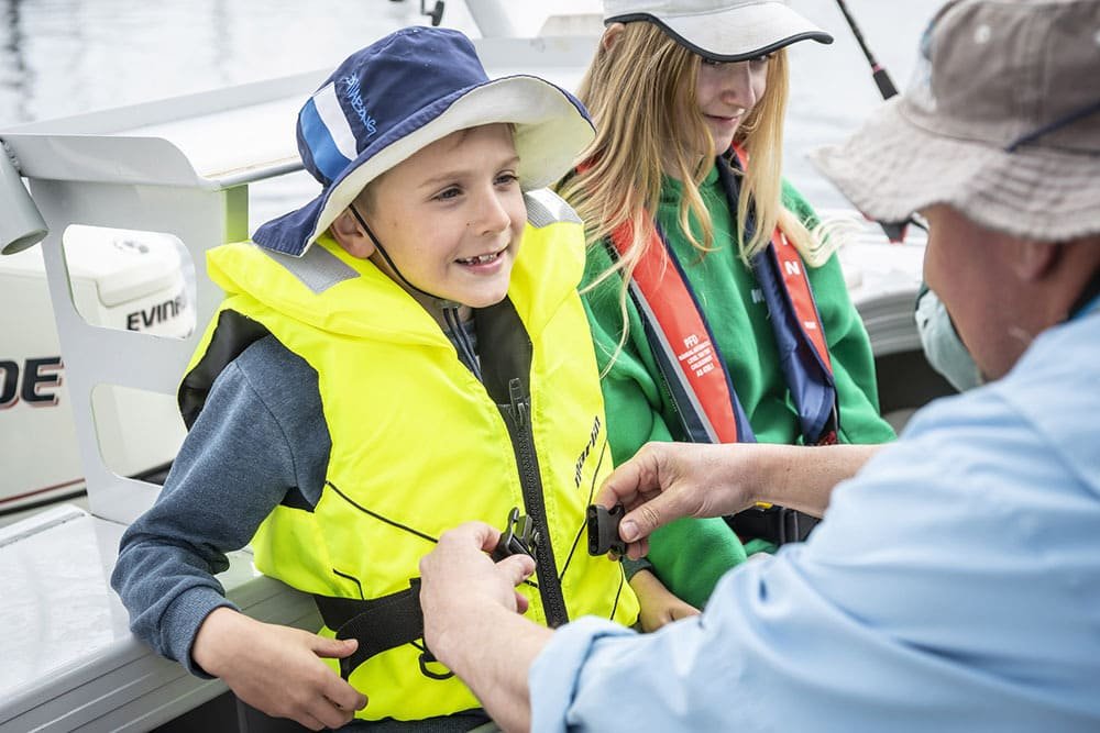 An adult helping children secure properly fitted foam life jackets